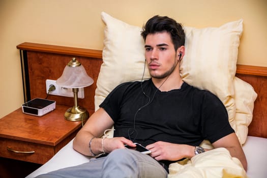 A young man laying in bed listening to music