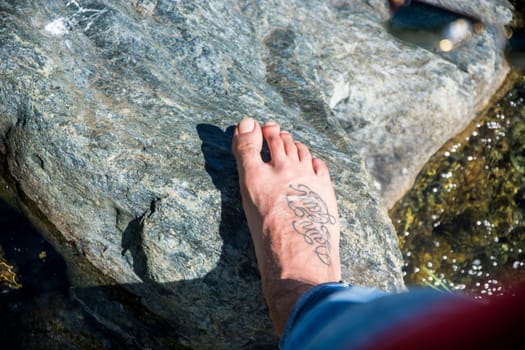 A person's foot on top of a rock next to a body of water