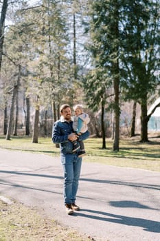 Smiling dad with a little girl in his arms walks along an asphalt road in a coniferous forest. High quality photo
