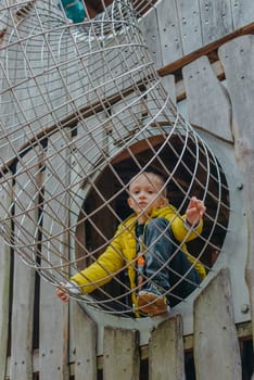 A child climbs up an alpine grid in a park on a playground on a hot summer day. children's playground in a public park, entertainment and recreation for children, mountaineering training. Child playing on outdoor playground. Kids play on school or kindergarten yard. Active kid on colorful slide and swing. Healthy summer activity for children. Little boy climbing outdoors.