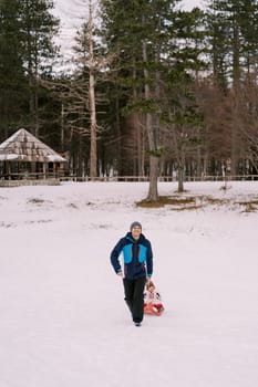 Dad is carrying a small child on a sleigh along the snowy plain at the edge of the forest. High quality photo