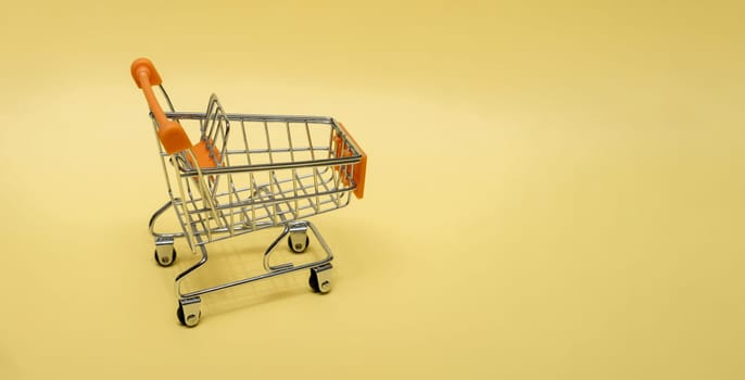 Small cart on a yellow background. Small supermarket grocery push cart for shopping. Shopaholic. Buyer. Shopping concept. Close-up. Isolated shopping trolley on a yellow background. Copy space.