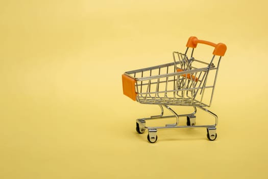 Small cart on a yellow background. Small supermarket grocery push cart for shopping. Shopaholic. Buyer. Shopping concept. Close-up. Isolated shopping trolley on a yellow background. Copy space.