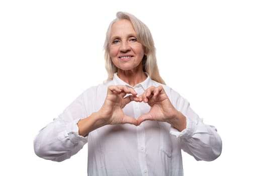 Portrait of a kind elderly business woman with gray hair in a shirt showing a heart with her hands.