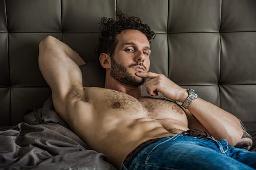 A man laying on top of a bed next to a pillow. A Laid-Back Hunk Resting on a Cozy Bed, Exuding Masculinity and Charm