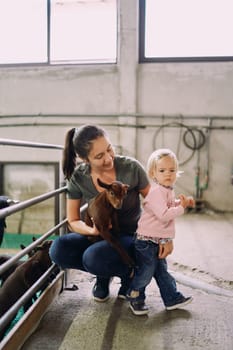 Little girl turns away from her mother with a little goat in her arms on a farm. High quality photo