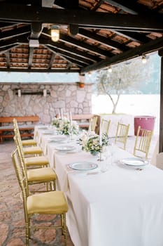 Golden chairs stand near a long festive table under a canopy in the garden. High quality photo