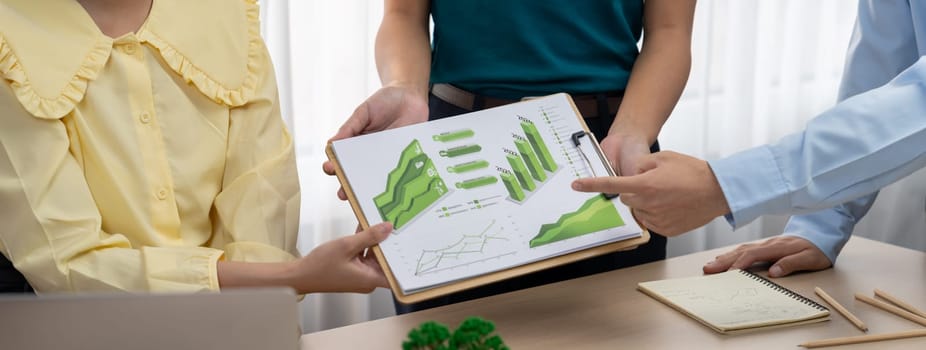 Professional business team presenting green business project by using graph to explain benefit of using renewable energy at modern meeting room. Closeup. Focus on hand. Delineation.