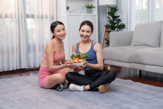 Young sporty Asian women in sportswear holding salad bowl together fill with vibrant of fruit and vegetable. Natural youthful and fit body lifestyle with balance nutrition and home exercise. Vigorous