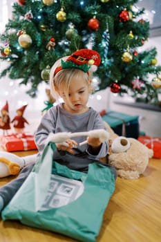 Little girl in a hoop with a gnome hat examines a hoop with cat ears, sitting by the Christmas tree. High quality photo