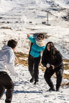 latin family at ski resort, in granada sierra nevada having fun throwing snowballs, playing on a sunny day,andalucia, spain,