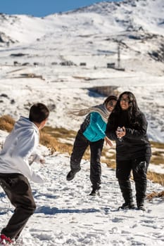 latin people, family in the snowy mountains of sierra nevada in granada, playing with the snow on a sunny day,andalucia, spain