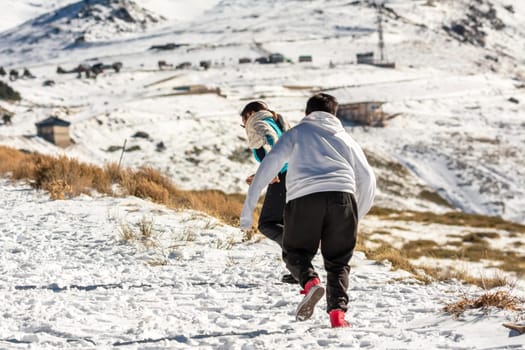 Latin mother and son running in the snow in Sierra Nevada Granada, Andalusia Spain