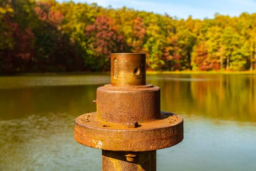 Close view of the rusty metal pipe and valve on a pier in calm reservoir in Coopers Rock State Forest near Morgantown, WV as the fall leaves provide the background