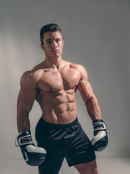 A muscular young man in studio with no shirt and boxing gloves