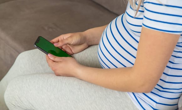 A pregnant woman plays on the phone on the Internet. Selective focus. Home.