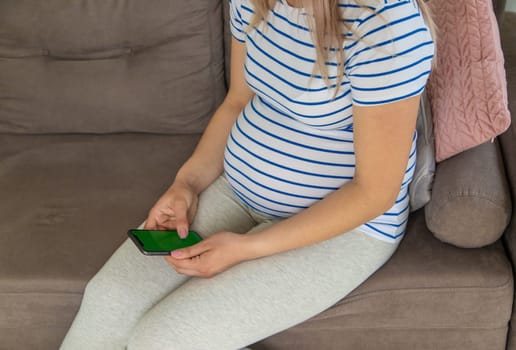 A pregnant woman plays on the phone on the Internet. Selective focus. Home.