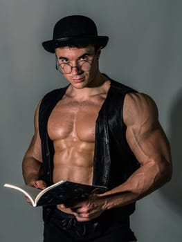 A man with a hat and glasses is holding a book. The Intellectual Hulk: A Muscular Man Embracing Knowledge and Fashion