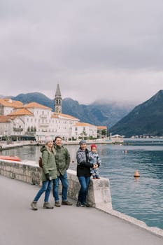 Man and woman are hugging near a mom with a little girl on the Perast embankment in winter. Montenegro. High quality photo