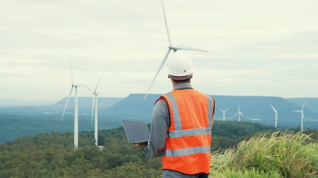 Engineer working on a wind farm atop a hill or mountain in the rural. Progressive ideal for the future production of renewable, sustainable energy. Energy generation from wind turbine.