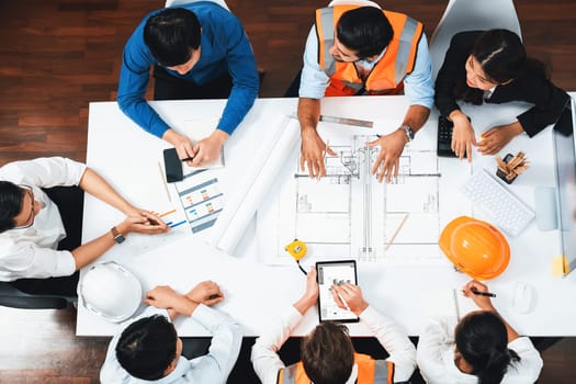 Top view banner of diverse group of civil engineer and client working together on architectural project, reviewing construction plan and building blueprint at meeting table. Prudent