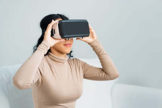 Young woman using virtual reality VR goggle at home for crucial online shopping experience. The virtual reality VR innovation optimized for female digital entertainment lifestyle.