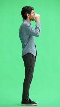 young man in full growth. isolated on green background. holding a mug of coffee.