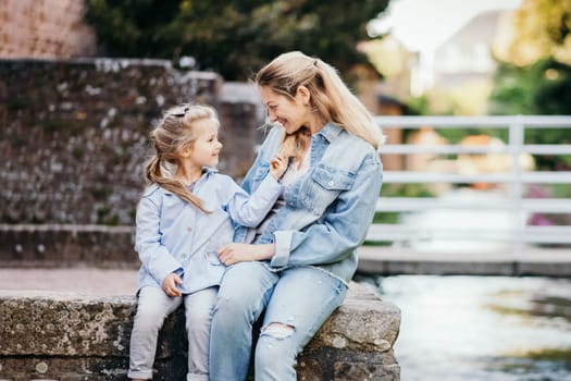 Mother and daughter sit near the river and laugh