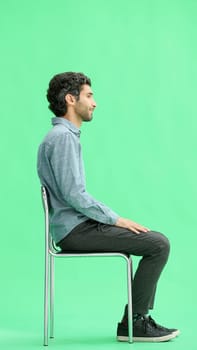 young man in full growth. isolated on a green background sitting on a chair.