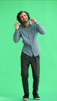 man in full growth. isolated on green background wearing headphones dancing.