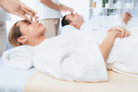 Caucasian couple enjoying relaxing anti-stress head massage and pampering facial beauty skin recreation leisure in dayspa modern light ambient at luxury resort or hotel spa salon. Quiescent
