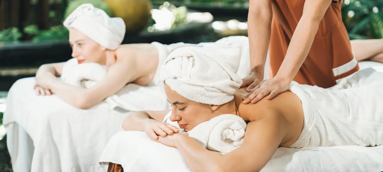 A portrait of two young attractive woman lie on bed during having back massage by a professional masseur at outdoor surrounded by peaceful natural environment. Healthy and beauty concept. Tranquility.