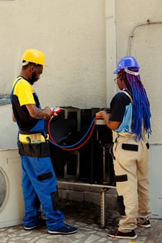 African american engineers hired after complaints about noisy air conditioner, and warm air coming from supply vents. Technicians using manometers to detect optimum fixing method