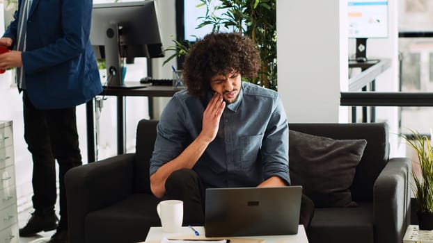 Dental inflammation in business office. Company employee suffering from toothache, cavity infection at work. Middle eastern man with caries feeling unwell in startup open space.