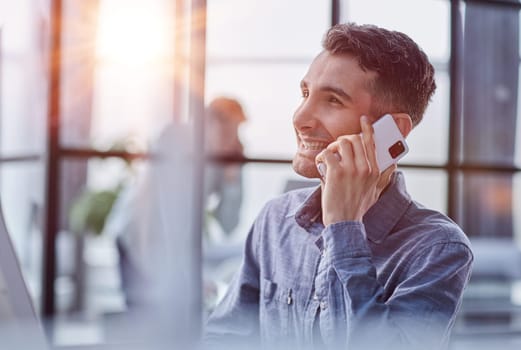 Portrait of young entrepreneur in casual office making phone call while working with laptop