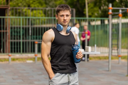 Portrait of athletic caucasian muscular man in sportswear holding drinking water bottle. Guy on playground before cardio workout exercises. Sports health fitness routine. Motivation. Outdoors gym