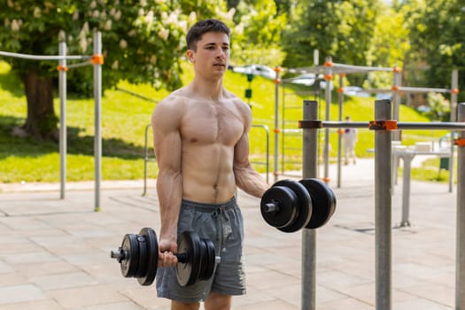 Athletic caucasian topless muscular man doing arms weight lifting dumbbells exercises, pumping up arm bicep muscles. Young guy on playground. Sports health fitness routine workout. Strength motivation