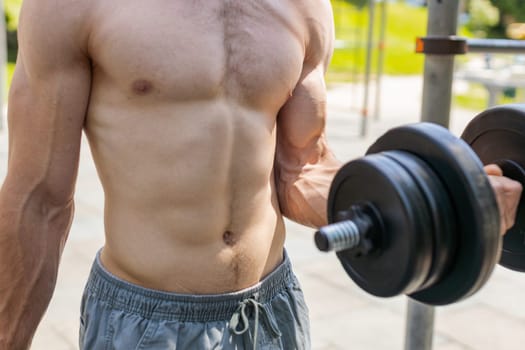 Close-up athletic topless muscular man doing arms weight lifting dumbbells exercises, pumping up arm bicep muscles. Guy on playground. Sports fitness routine, bodybuilding workout. Strength motivation