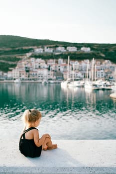 Little girl sits barefoot on the pier and looks at the sea. Back view. High quality photo