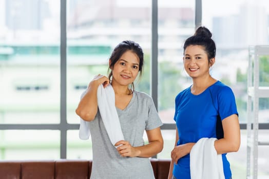 Asian adult and young woman smiling with towel around neck after yoga and exercise. Portrait of happy beautiful female standing indoor yoga studio, sport healthy workout concept