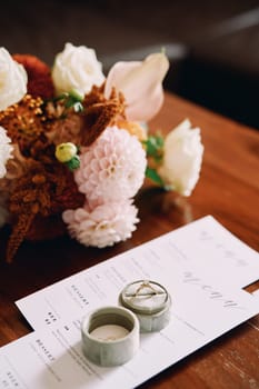 Engagement ring in a box stands on a festive menu on a wooden table near a bouquet. High quality photo
