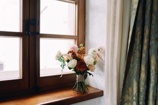 Bride bouquet stands on a wooden windowsill near the curtains. High quality photo