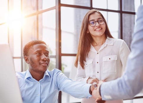 Cheerful multiracial colleagues discussing startup project and smiling during workday in office interior