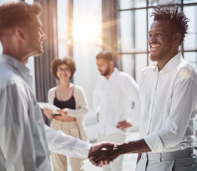 Glad to work with you. Young modern men in smart casual wear shaking hands and smiling while working in the creative office