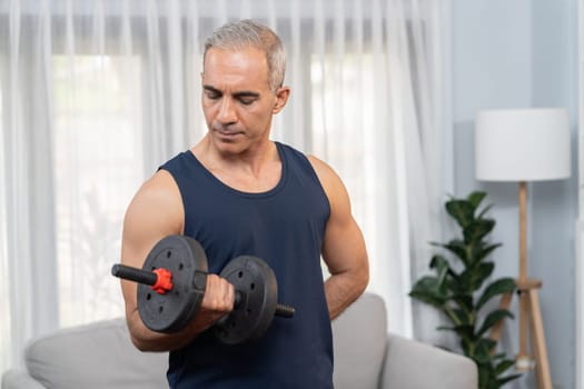 Athletic and sporty senior man engaging in body workout routine with lifting dumbbell at home as concept of healthy fit body with body weight lifestyle after retirement. Clout