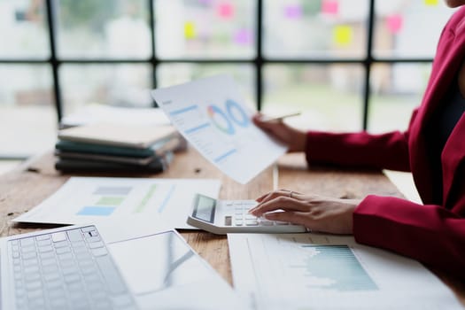 businesswoman or accountant working on calculator and laptop computer to calculate business data during using accountancy document at office.