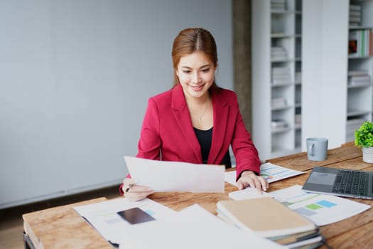 businesswoman or accountant working on calculator and laptop computer to calculate business data during using accountancy document at office.