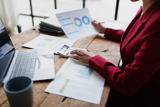 businesswoman or accountant working on calculator and laptop computer to calculate business data during using accountancy document at office.