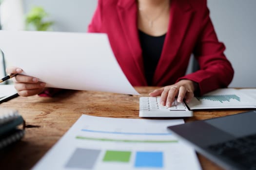 businesswoman or accountant working on calculator and laptop computer to calculate business data during using accountancy document at office.