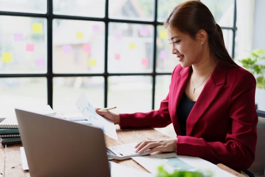 businesswoman or accountant working on calculator and laptop computer to calculate business data during using accountancy document at office.